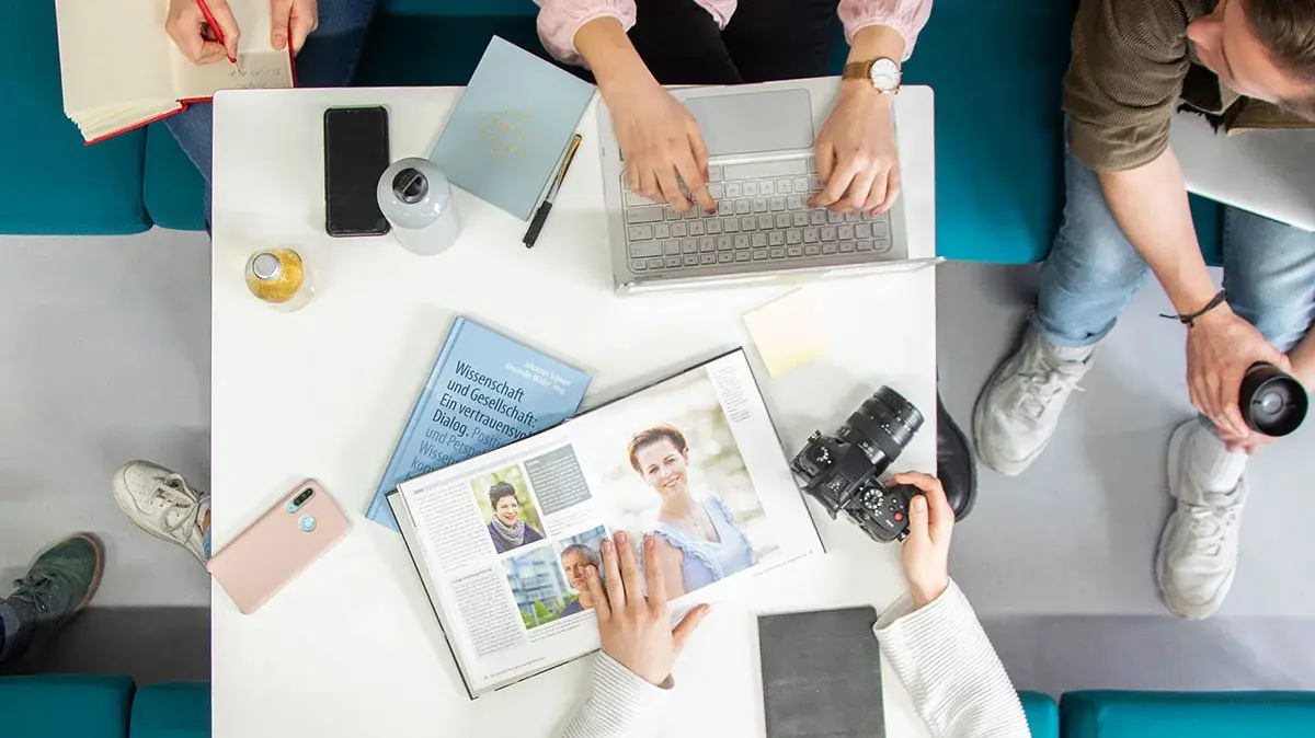 Studenten Crossmedia-Redaktion/Public Relations arbeiten gemeinsam an einem Tisch im edit.Lab, der Lehrredaktion des Studiengangs. Die Aufnahme ist von oben.