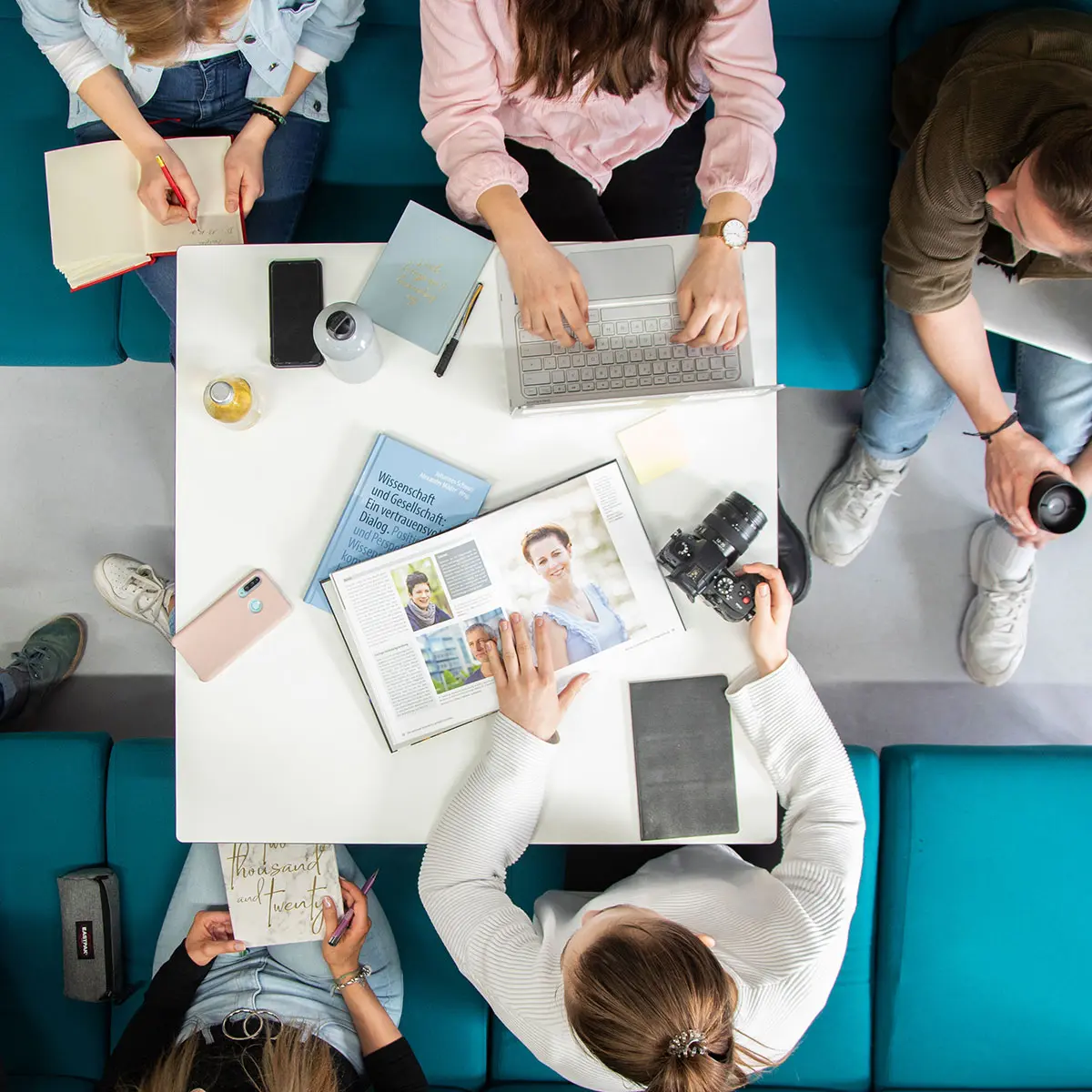 Studenten Crossmedia-Redaktion/Public Relations arbeiten gemeinsam an einem Tisch im edit.Lab, der Lehrredaktion des Studiengangs. Die Aufnahme ist von oben.