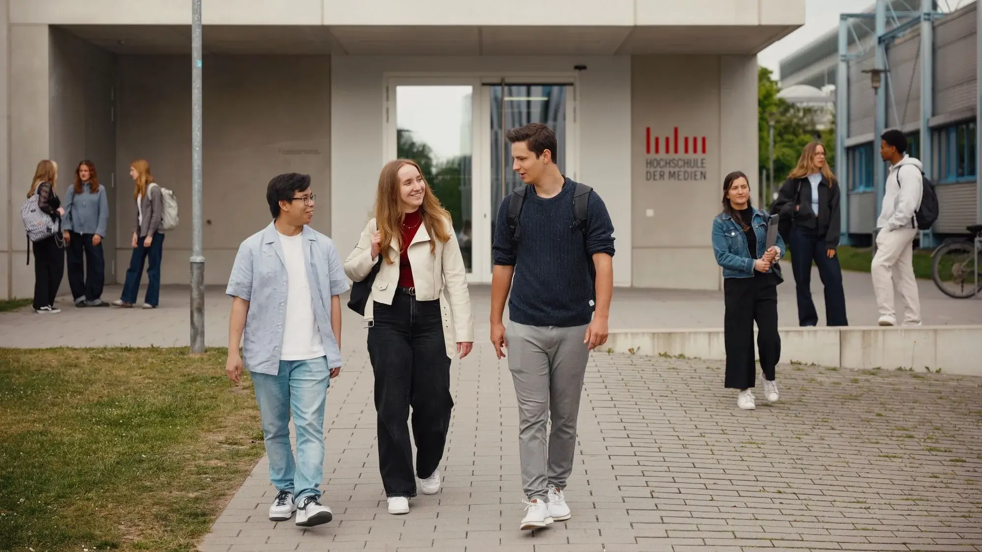 Studierende unterhalten sich beim Laufen vor dem HdM Gebäude