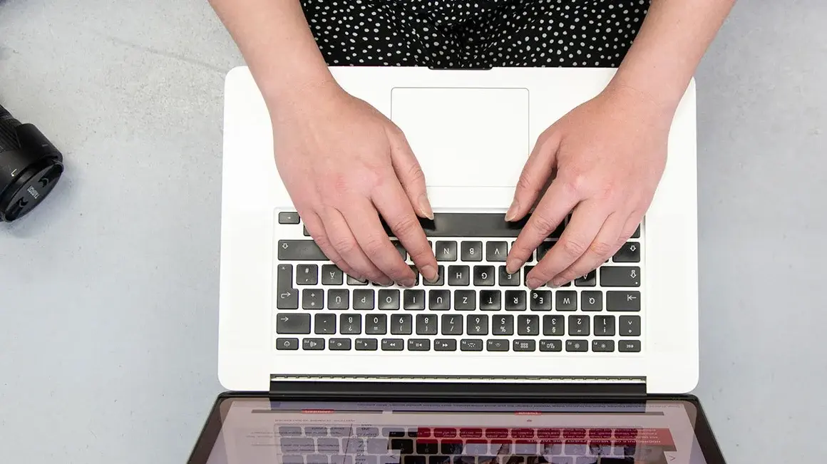 Studentin Crossmedia-Redaktion/Public Relations tippt auf Laptop zu sehen von oben.