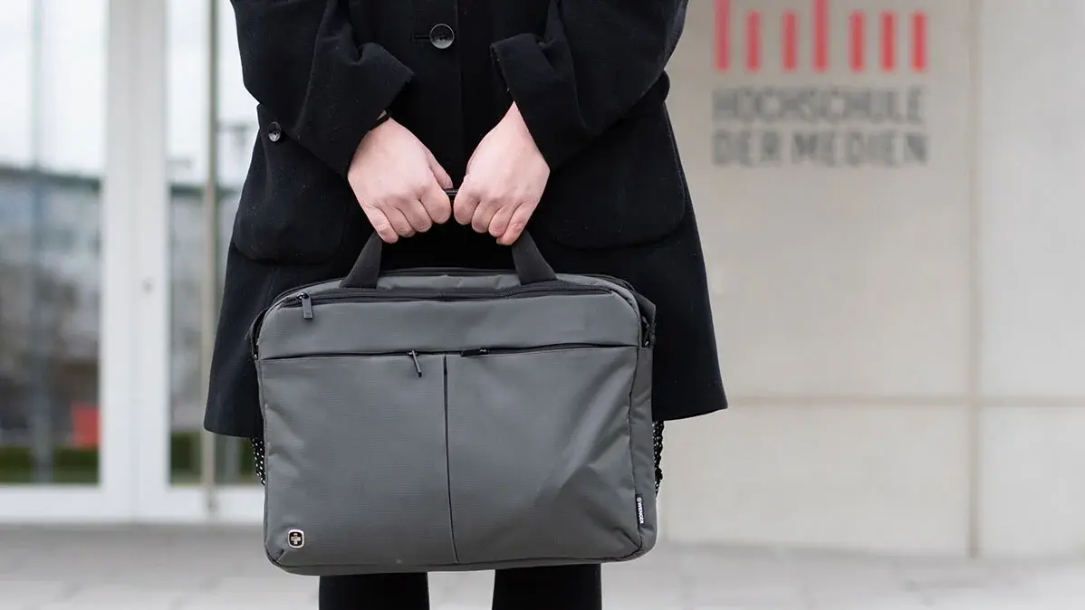 Studentin Crossmedia-Redaktion/Public Relations steht mit Laptoptasche vor dem HdM Gebäude. Zu sehen ist das HdM Logo am Gebäude im Hintergrund.