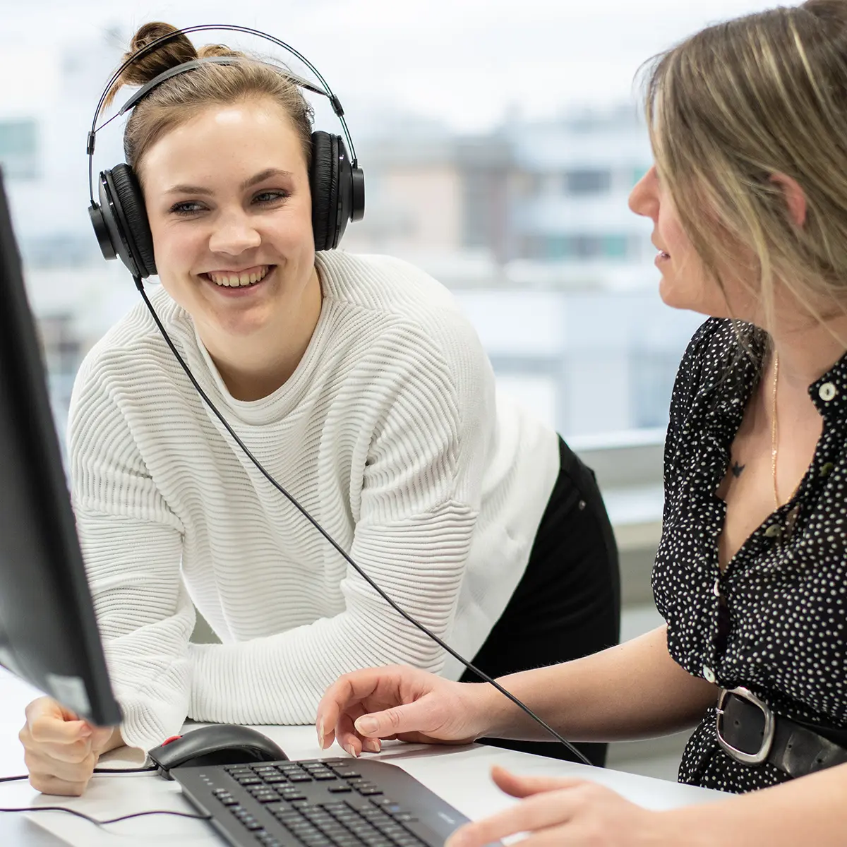 Studierende Crossmedia-Redaktion/Public Relations arbeiten gemeinsam an einem Videoschnittprojekt im edit.Lab, der Lehrredaktion des Studiengangs. Eine Studentin hat einen Kopfhörer auf.