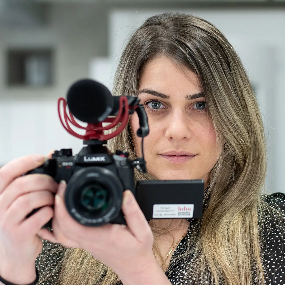 Studentin Crossmedia-Redaktion/Public Relations hält Kamera mit Mikrofon auf Betrachter geichtet und schaut uns direkt an.